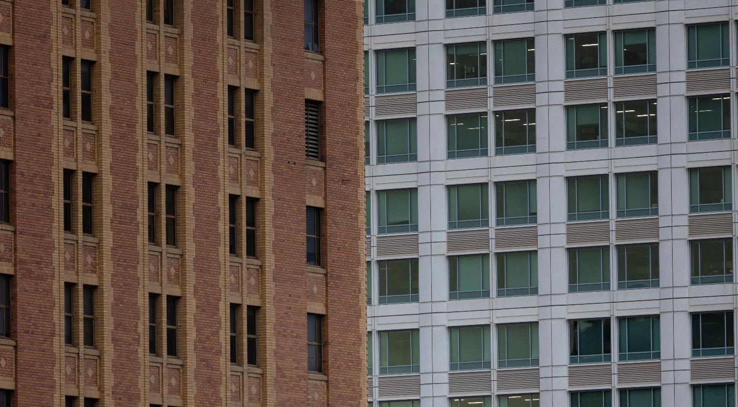 Contrast of a brick historic building facade next to a modern glass office tower, representing decades of Philadelphia commercial real estate redevelopment.