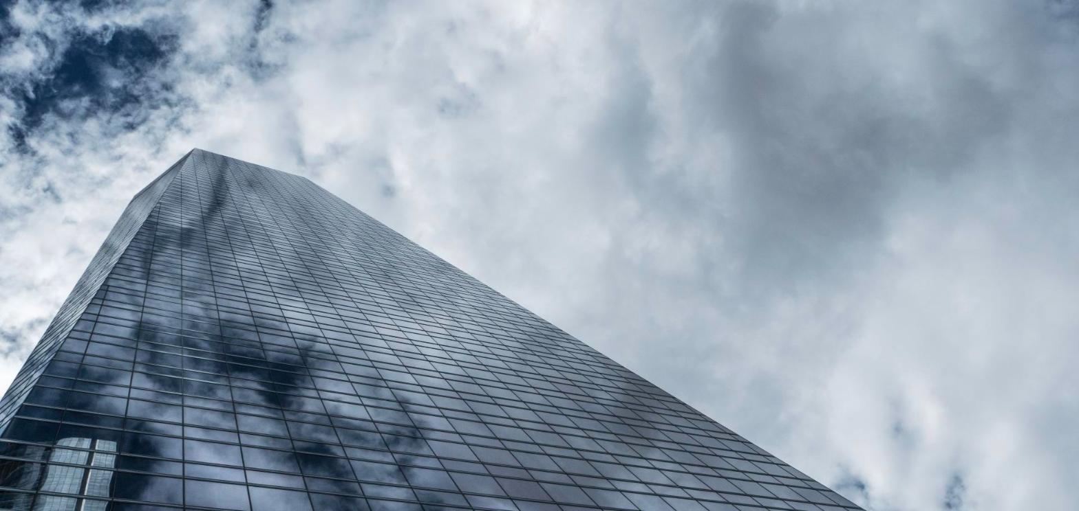 Low angle view of a glass office tower against a cloudy sky, representing a Philadelphia office landlord's disposition strategy.
