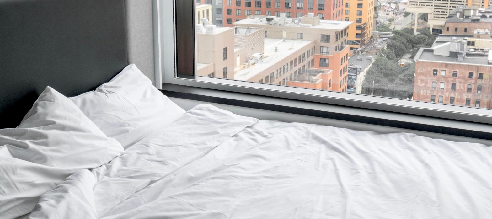 Hotel bed beside a window overlooking a city skyline, representing a Center City hotel stay.