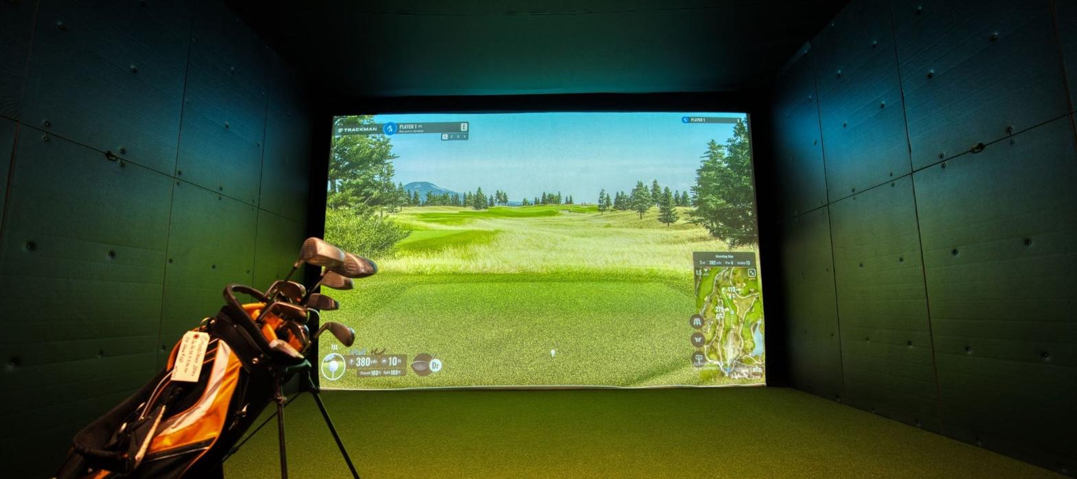 Indoor golf simulator bay with a projected course on screen, representing a Trackman simulator lounge.