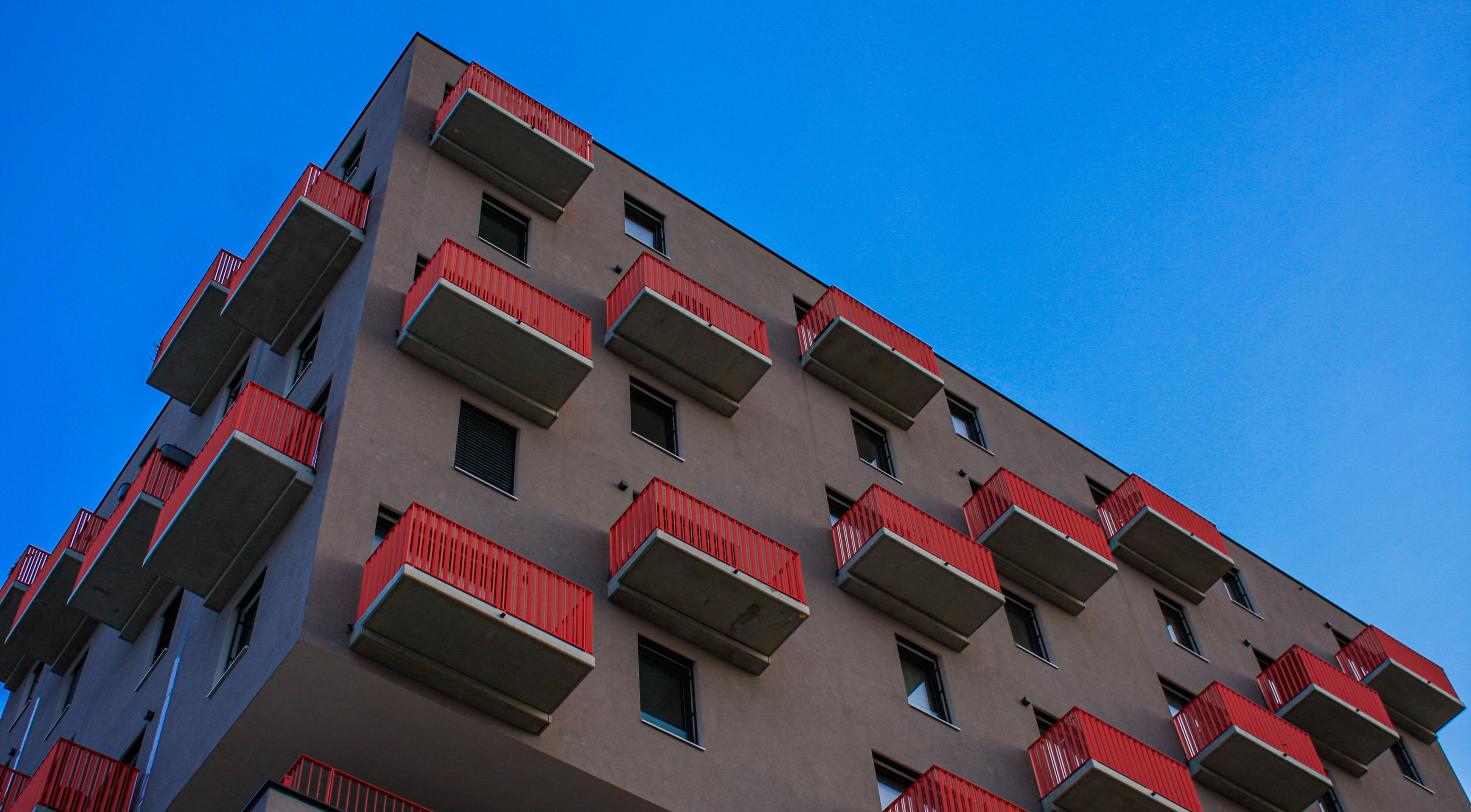 Modern apartment building facade with red balconies, representing a new multifamily development replacing an office building.