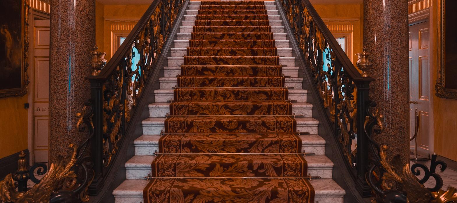 Grand historic mansion staircase with ornate railings, representing a Gilded Age estate restoration.