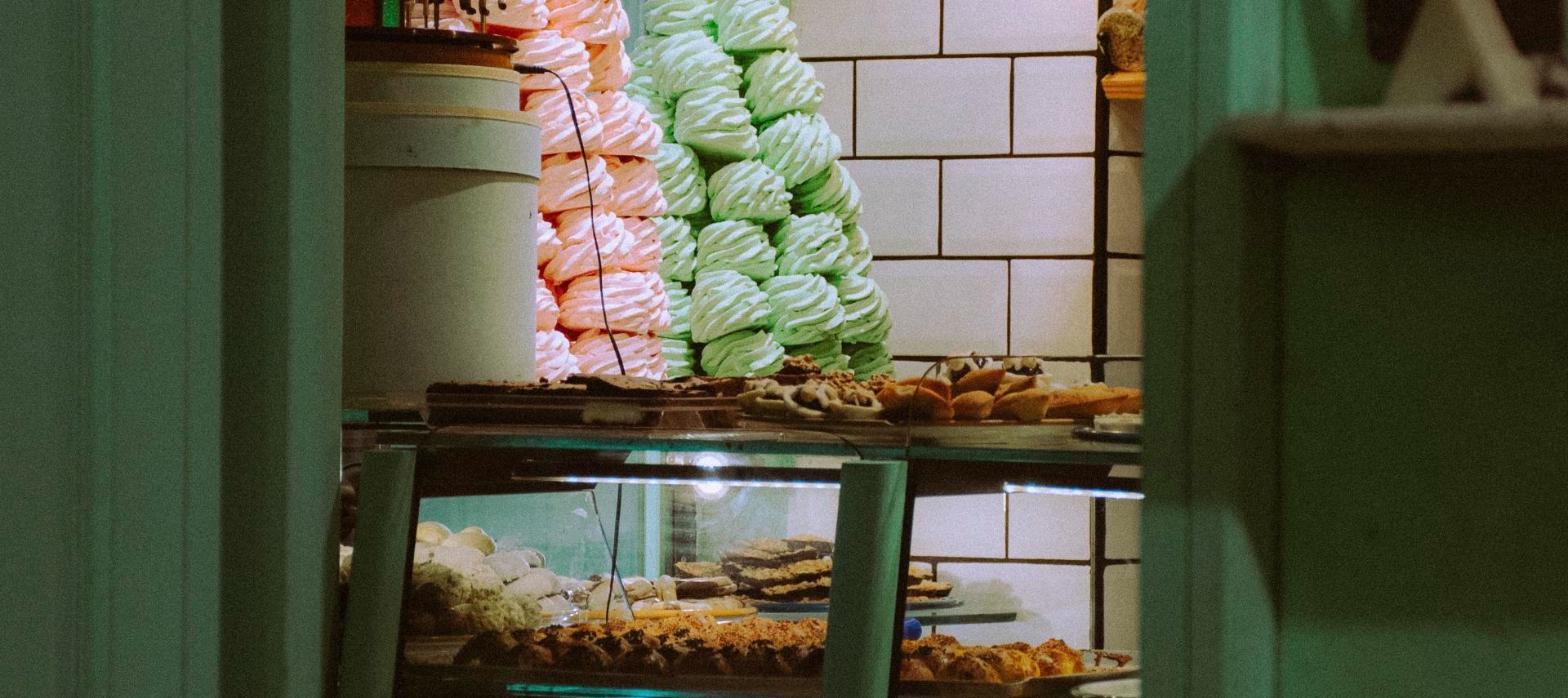Pastel pastries and macarons stacked in a green-tiled bakery display, representing a bakery storefront.