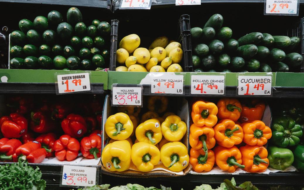 Colorful produce display of peppers, squash and cucumbers at a grocery store, representing a grocery-anchored shopping center.
