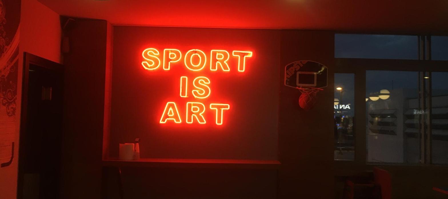 Red neon sign glowing inside a dimly lit sports bar with a mounted basketball hoop, representing a women's sports bar closing on South Street.