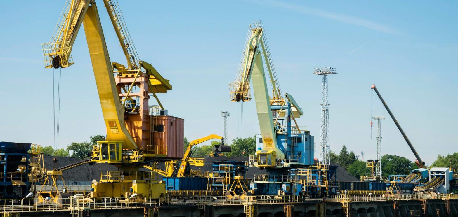 Industrial dockside cranes at a river port, representing a port terminal expansion.