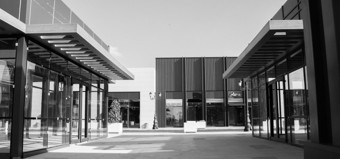 Black and white photo of a modern retail plaza with glass storefronts and covered walkways, representing a multi-property retail portfolio sale.