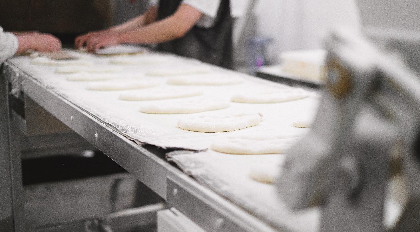 Rows of dough on a bakery production line, representing a food manufacturing facility.
